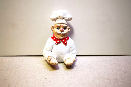 Small figurine of a chef with a white hat and red scarf on a beige background